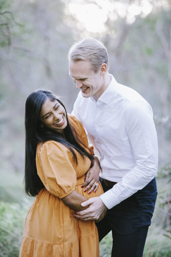 pregnant mum holding her belly during laughing with her husband in a maternity photography session in Perth