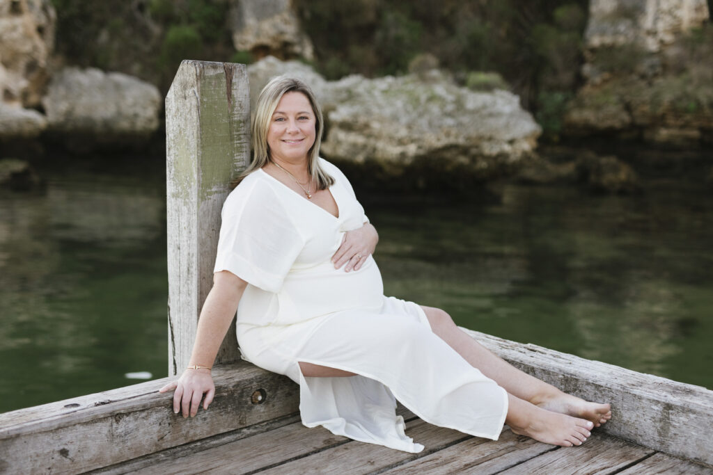 Pregnant mother in a white dress sitting on a timber jetty during a maternity photography session at Bay View Park, Mosman Park, Perth.
