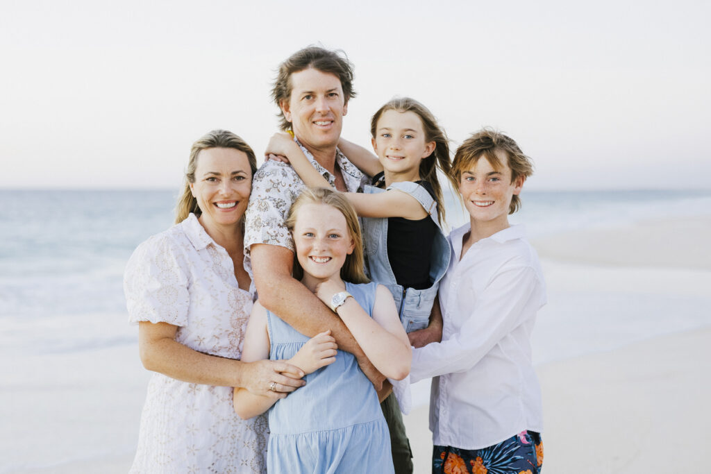 Family of five smiling together on the shoreline during a sunset family photography session at City Beach, Perth.