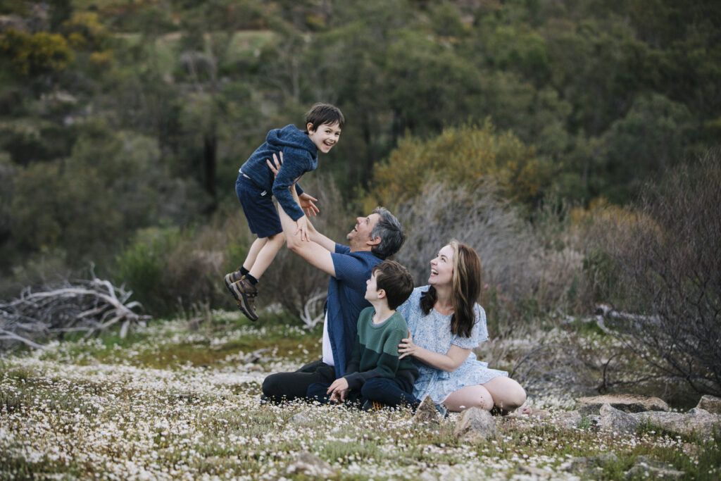 Family photography session at Hovea Falls in Perth with parents playing and laughing with their two sons among wildflowers