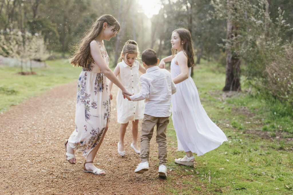 Children holding hands and playing together on a forest track during a family photography session in Jarrahdale Forest near Perth.