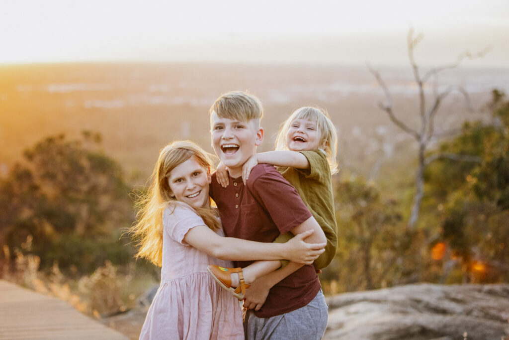 Children hugging and laughing together during a family photography session at Lesmurdie Falls in the Perth Hills at sunset.