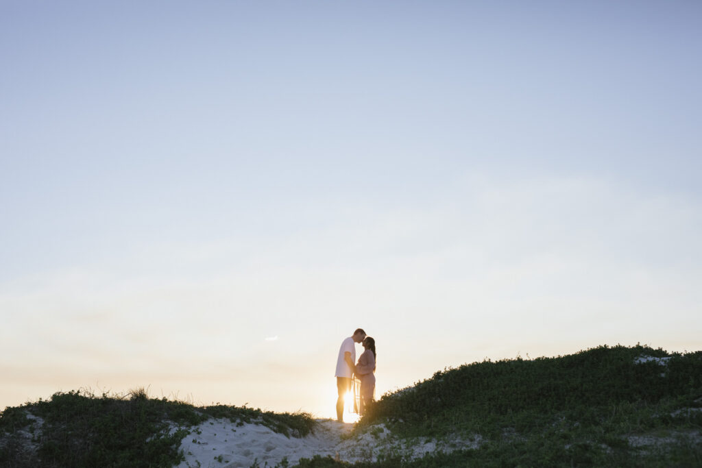 Expectant couple sharing a sunset moment on the sand dunes during a maternity photography session at Mullaloo Beach, Perth.