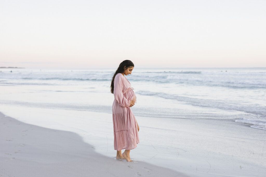 Pregnant woman walking along the shoreline during a relaxed maternity photography session at Mullaloo Beach, Perth.