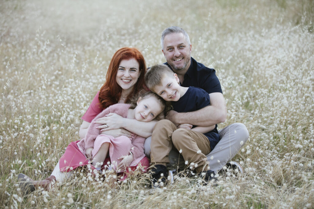 Family of four sitting together in a wildflower field during a relaxed outdoor family photography session at Perry's Paddock, Floreat, Perth.