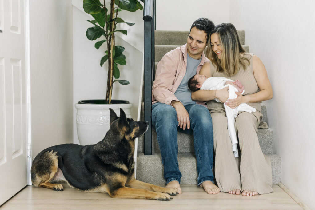 Family relaxing on the stairs at home with their newborn and loyal dog during a natural in-home newborn photography session in Perth.