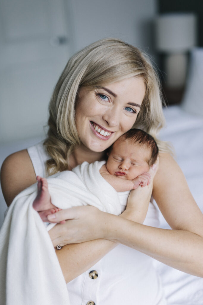 Smiling mum holding her sleeping newborn during a relaxed in-home baby photography session in Perth.