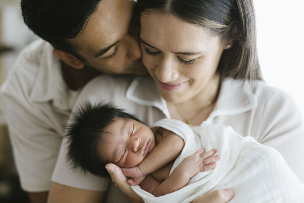 Parents sharing a quiet moment with their sleeping newborn during an in-home newborn photography session in Perth.