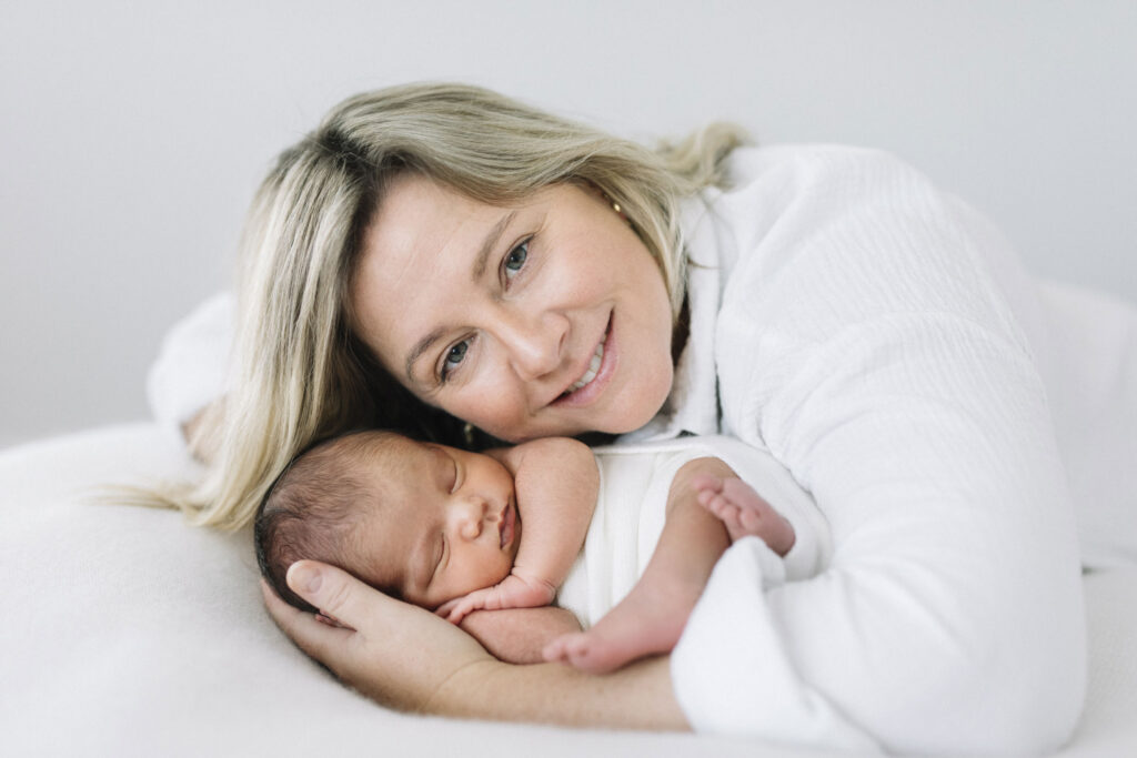 Natural motherhood portrait during an mosman park in-home newborn photography session in Perth, with mum cuddling her sleeping newborn on the bed.