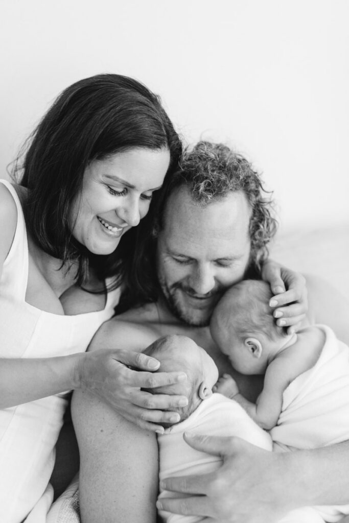 Parents cuddling their newborn twins during a relaxed in-home newborn photography session in Perth, capturing the connection between the whole family.
